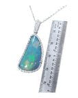 Australian opal pendant with blue-green play of color, halo diamonds, and 18K white gold chain, next to a ruler.
