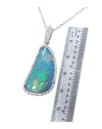 Australian opal pendant with blue-green play of color, halo diamonds, and 18K white gold chain, next to a ruler.