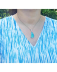 Australian opal pendant with blue-green play of color, halo diamonds, 18K white gold, worn on a woman.