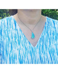 Australian opal pendant with blue-green play of color, halo diamonds, 18K white gold, worn on a woman.