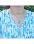 Australian opal pendant with blue-green play of color, halo diamonds, 18K white gold, worn on a woman.