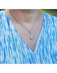 Person wearing a blue and white patterned top with a necklace featuring a teardrop opal pendant.