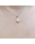 Oval white Australian opal pendant in 14k yellow gold on a delicate chain, worn on a person.