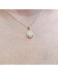 Oval white Australian opal pendant in 14k yellow gold on a delicate chain, worn on a person.