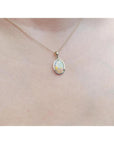 Oval white Australian opal pendant in 14k yellow gold on a delicate chain, worn on a person.