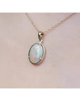 1.92 ct. oval white opal pendant in 14k yellow gold on a delicate chain, worn on a person.