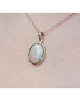 1.92 ct. oval white opal pendant in 14k yellow gold on a delicate chain, worn on a person.