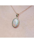 1.92 ct. oval white opal pendant in 14k yellow gold on a delicate chain, worn on a person.