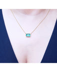 East-west rectangular emerald solitaire necklace in 18K yellow gold, worn on a person.