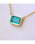 East-west emerald-cut Colombian emerald solitaire necklace in 18K yellow gold.