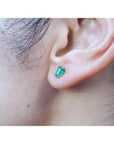 Emerald cut emerald stud earring in 14K yellow gold on an earlobe.