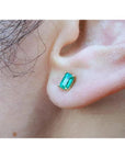 An ear wearing a Colombian emerald solitaire stud earring in 14k gold.
