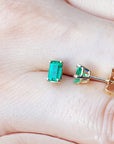 14k Yellow gold emerald solitaire stud earrings on a hand.