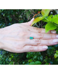 Pair of emerald cut emerald stud earrings in 14K yellow gold, displayed on a hand.