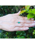 Pair of emerald cut emerald stud earrings in 14K yellow gold, displayed on a hand.