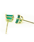 Pair of emerald gemstone earrings with gold settings on a side profile view.