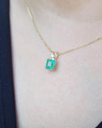 Gold necklace with a square emerald pendant on a person wearing a dark top.