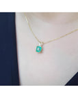 Emerald-cut emerald pendant in 14K yellow gold with diamond accent, worn on a woman's neck.