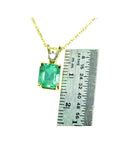 Gold pendant with a natural emerald-cut emerald next to a ruler for size reference on a white background.