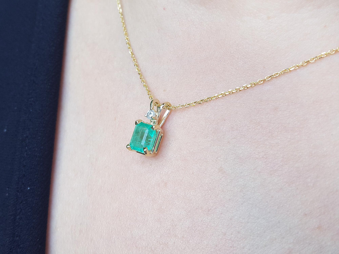 Gold necklace with a Muzo colombian emerald pendant on a person's neck.