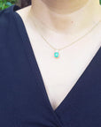 A woman wearing a navy-blue top with a gold necklace featuring a natural emerald pendant.