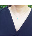 A woman wearing a navy-blue top with a gold necklace featuring a natural emerald pendant.