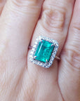 Emerald ring for women with halo diamond on a person's finger.