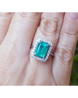 A colombian emerald ring for women adorned with a halo diamond on a person's finger.