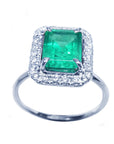 Ring with emerald and halo diamond in white gold on a white background.