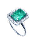 White gold women's emerald ring with halo diamond on a topside profile view.