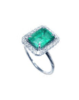 White gold women's emerald ring with halo diamond on a topside profile view.