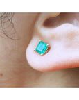 14k yellow gold square natural colombian emerald stud earring on an earlobe.