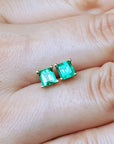Genuine emerald stud earrings held between fingers.