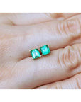 Pair of square emerald stud earrings in 14K yellow gold, worn on an earlobe.