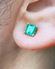 Square emerald stud earring on a person's ear.