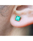 Square emerald stud earring in 14K yellow gold, worn on an ear.