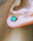 Close-up of an emerald gemstone earring on a person's ear.