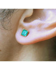 Square emerald stud earring in 14K yellow gold, worn on an ear.