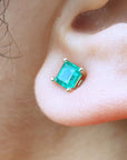 Close-up of a yellow gold square emerald stud earring on an earlobe.