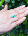Hand displaying a square Colombian emerald stud earrings against a green leafy background.