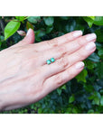 14K yellow gold square emerald stud earrings on a hand, surrounded by green leaves.