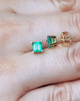 Square emerald stud earrings on a hand.