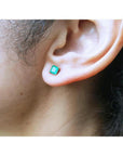 Square emerald stud earring in 14K yellow gold on an earlobe.