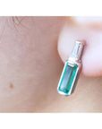 Close-up of a baguette cut emerald stud earring on a person's ear.