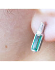 Close-up of a baguette cut emerald stud earring on a person's ear.