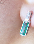 Close-up of a baguette cut emerald stud earring on a person's ear.