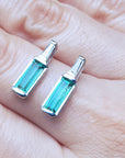 Two natural baguette emerald stud earrings on a hand.