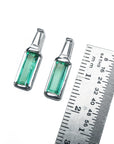 Two Muzo Colombian baguette emerald stud earrings next to a ruler for scale on a white background