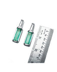 Two Muzo Colombian baguette emerald stud earrings next to a ruler for scale on a white background