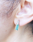 Close-up of an ear wearing an emerald stud earring with a blurred background